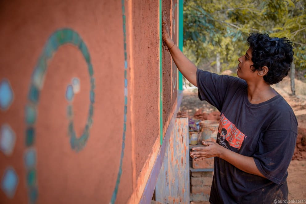 1 Nikki mud plastering a wall in Anitya community