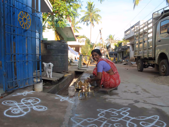 A village lady washes puja items on the street